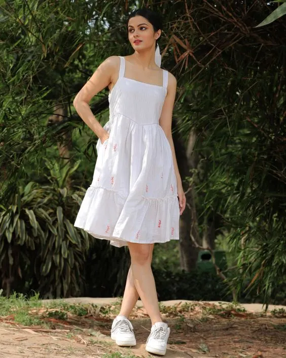 A woman dressed in a white dress and sneakers, showcasing a blend of comfort and style in a vibrant outdoor scene.