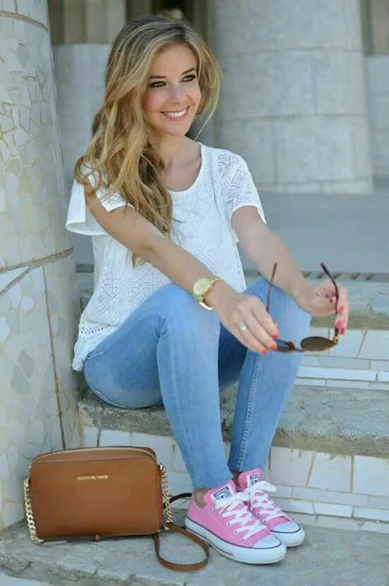 A young woman in stylish jeans and sneakers sits on steps, embodying a blend of beauty and casual fashion.