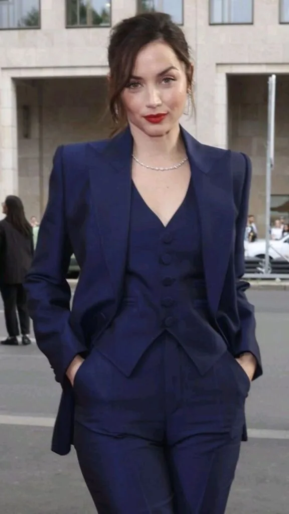 A woman wearing a blue suit and red lipstick, exuding confidence and professionalism in a stylish pose.
